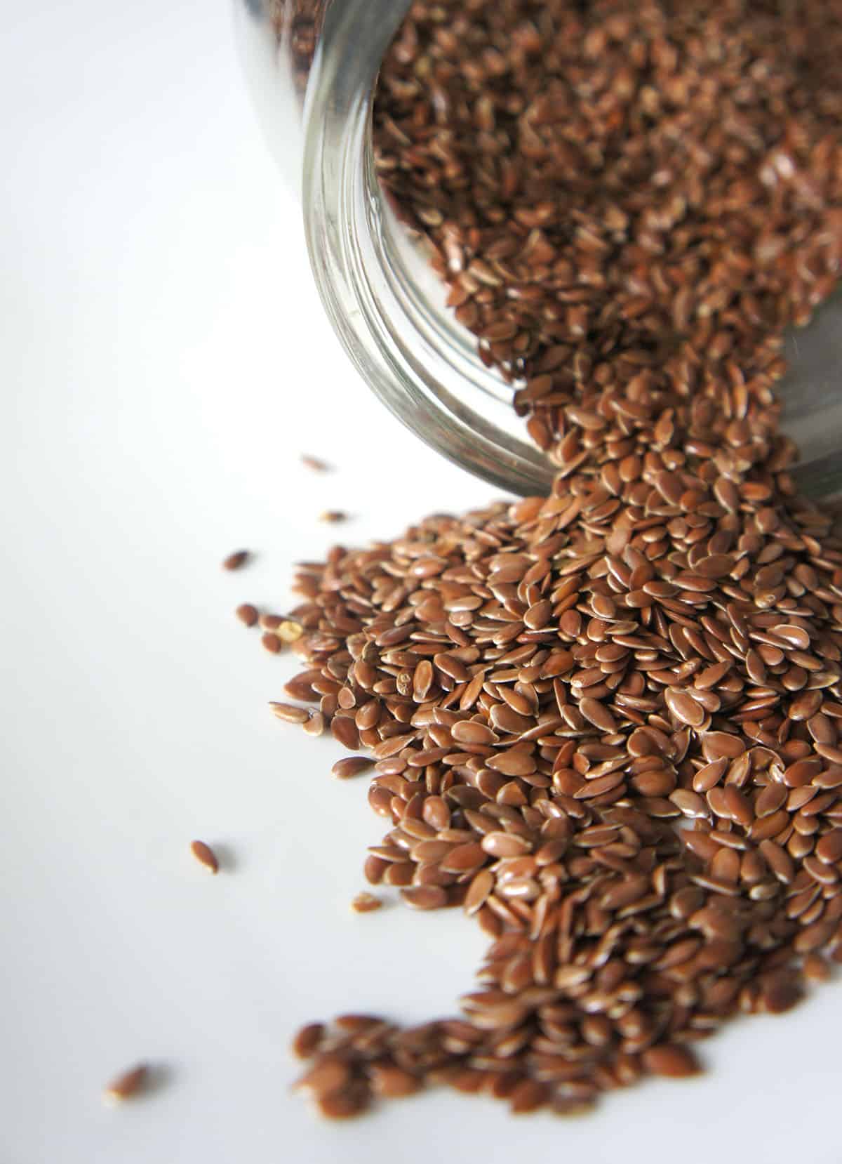 flax seeds spilling out of a glass container onto a white background - vegan pantry staple # 5