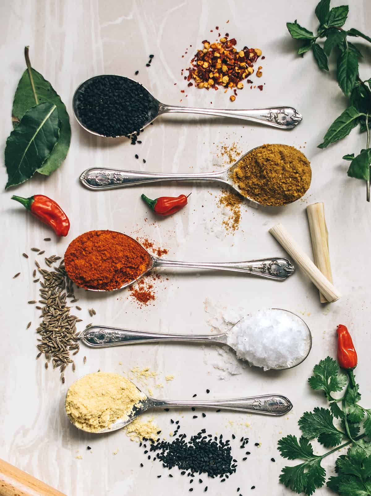 herbs and spices on spoons and white table