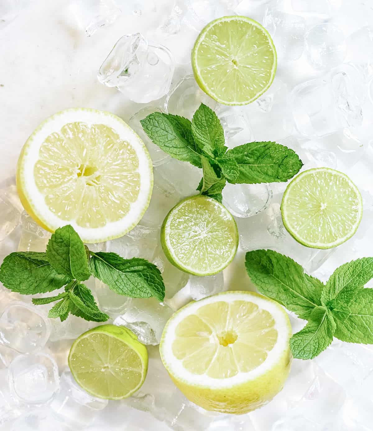 lemons and limes on a white table with ice and mint