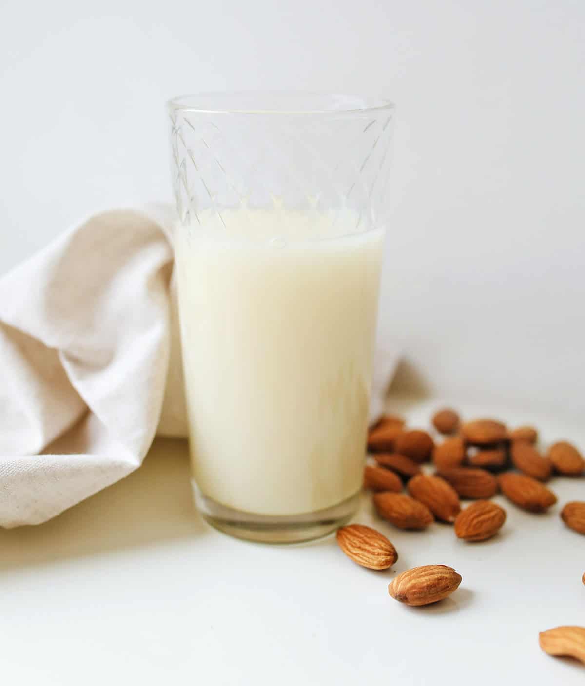 clear glass of almond milk on a white background with a handful of almonds and a white linen - first vegan pantry item