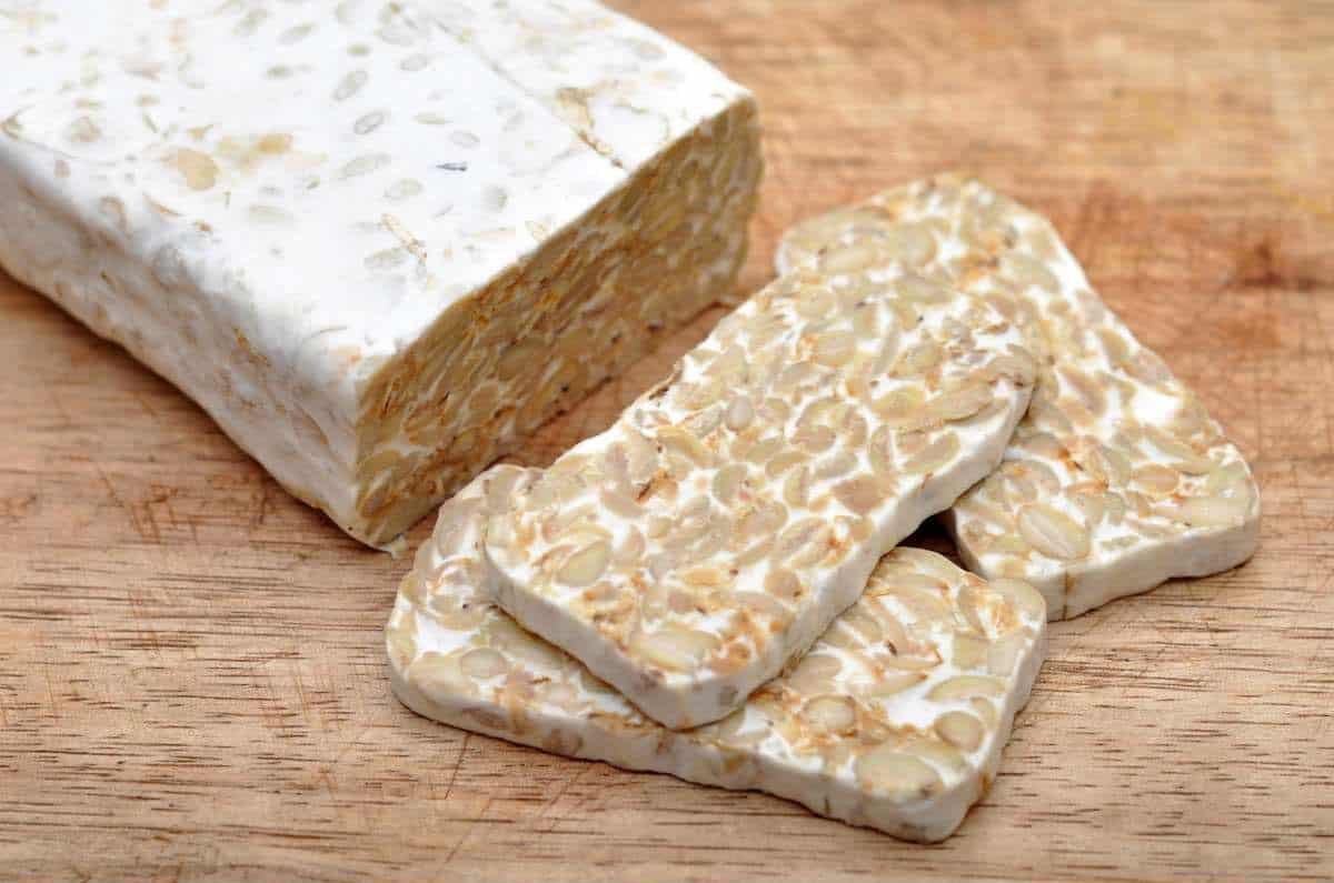 block of tempeh with some slices cut off on a wooden cutting board