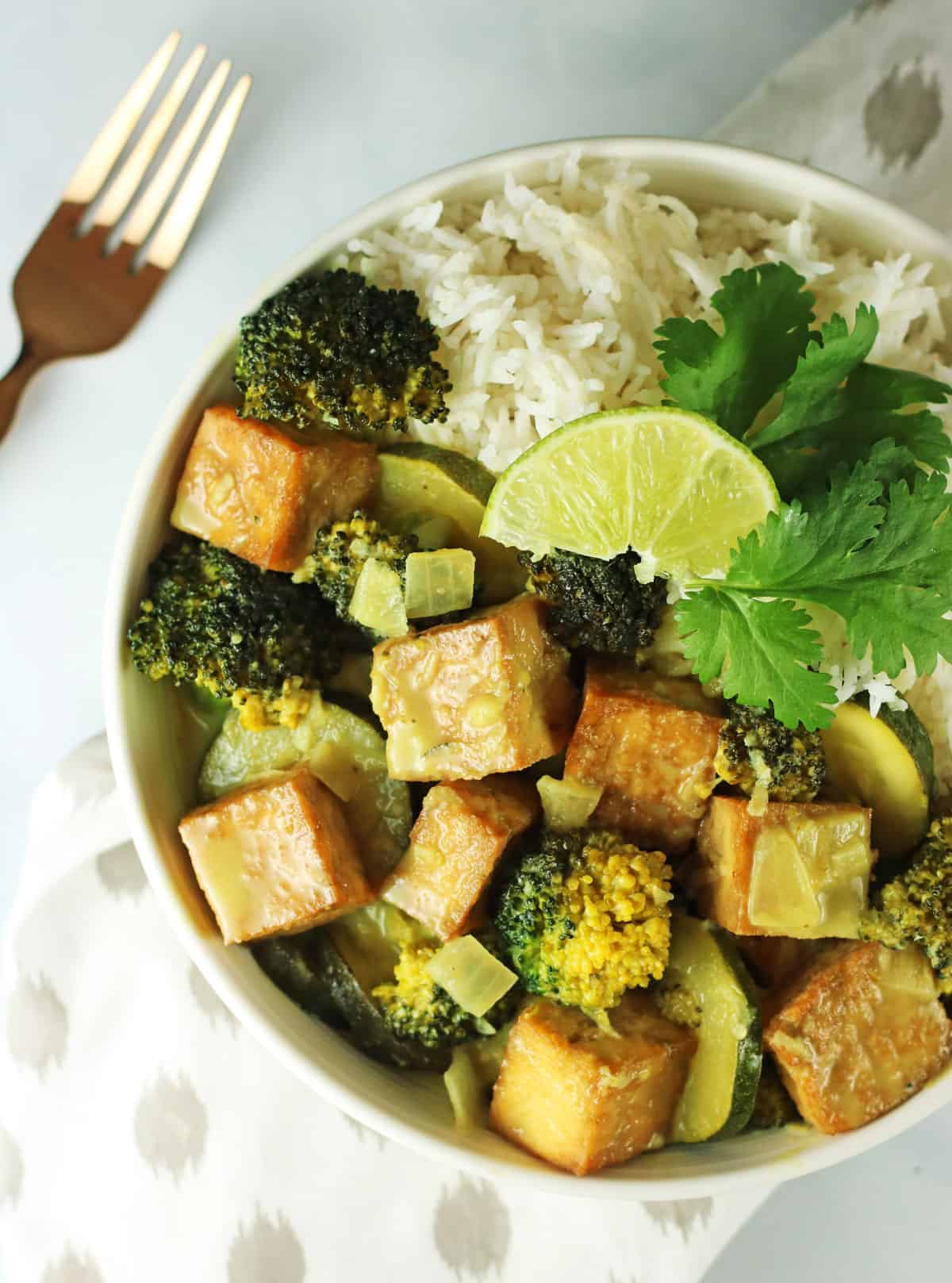 overhead shot of green curry with mixed vegetables and tofu with white rice.