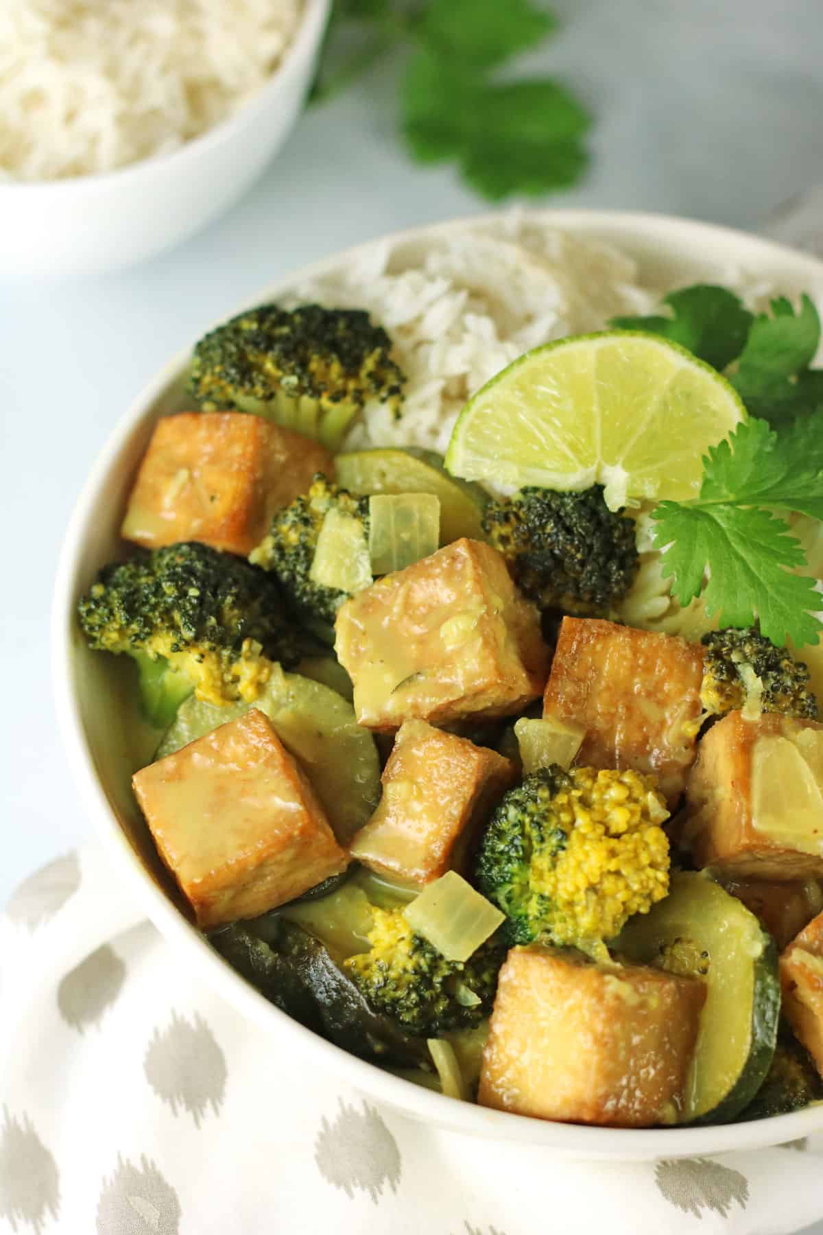 crispy tofu green curry in a white bowl with a slice of lime.