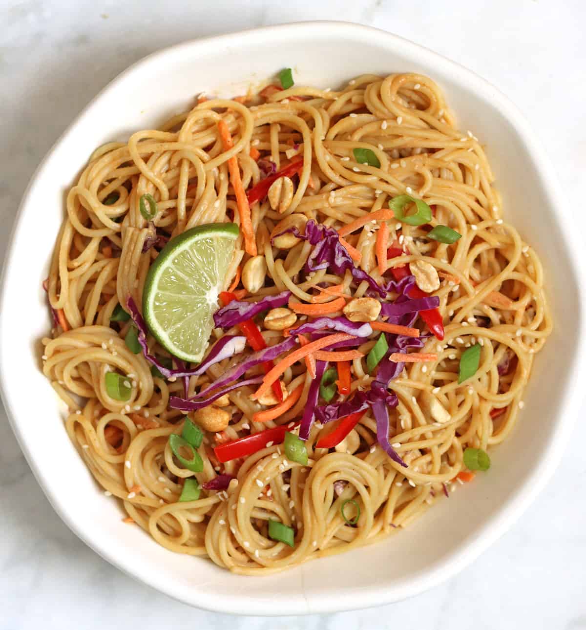 vegan peanut noodles in a bowl with assorted veggie and nut toppings.