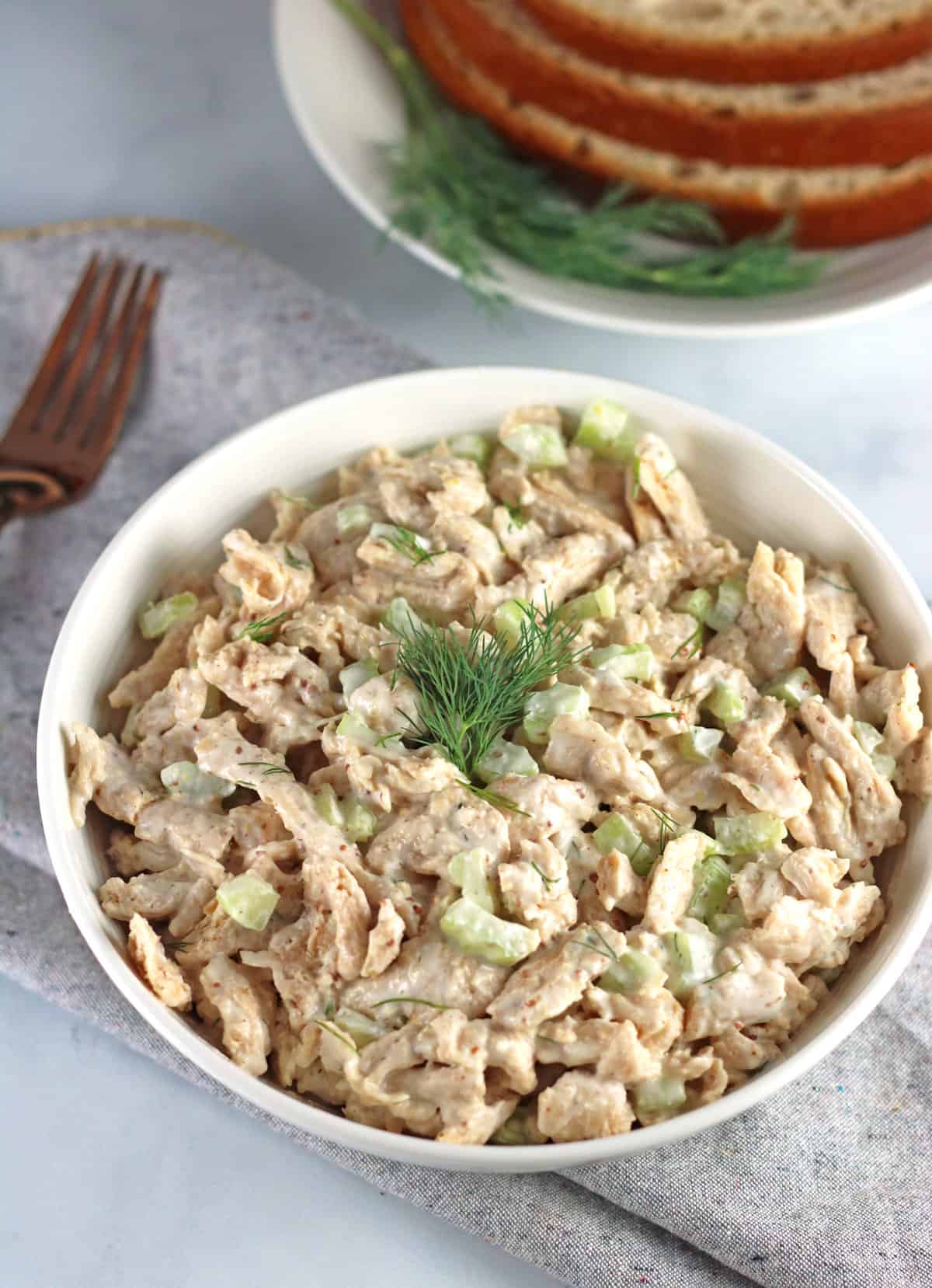 vegan chicken salad in a bowl with dill and slices of bread and a gold fork in the background.