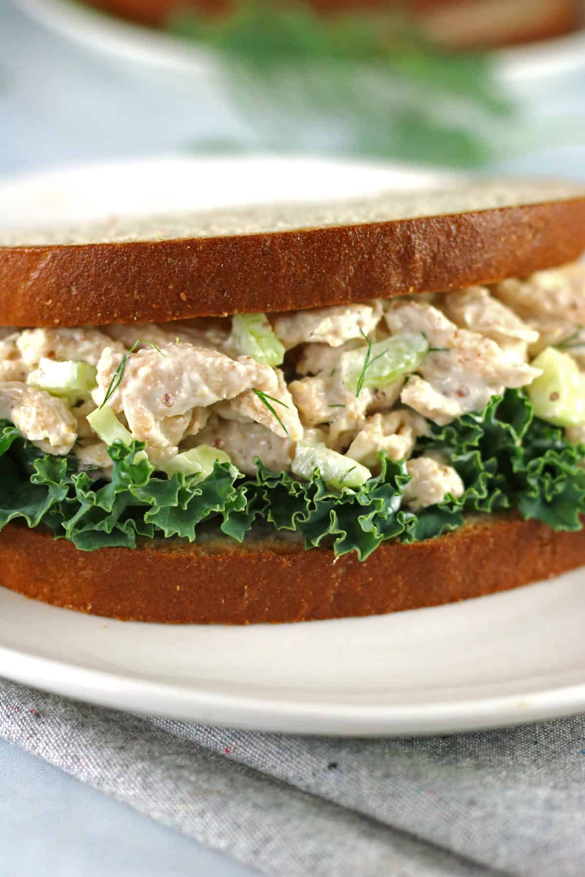 closeup of vegan chicken salad in a sandwich with lettuce on a white plate and gray napkin.