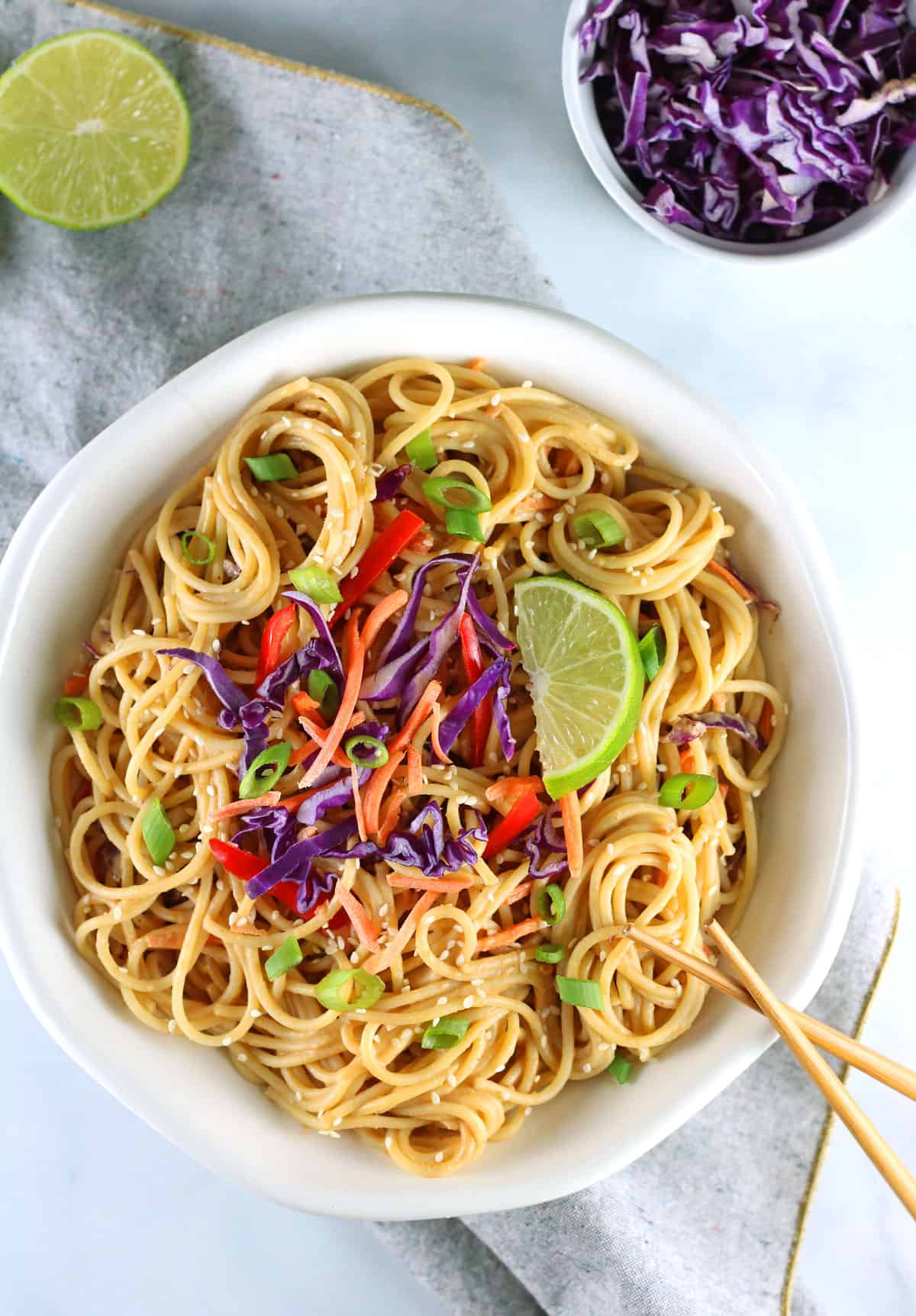 vegan peanut sauce noodles overhead shot with lime, cabbage and chopsticks.