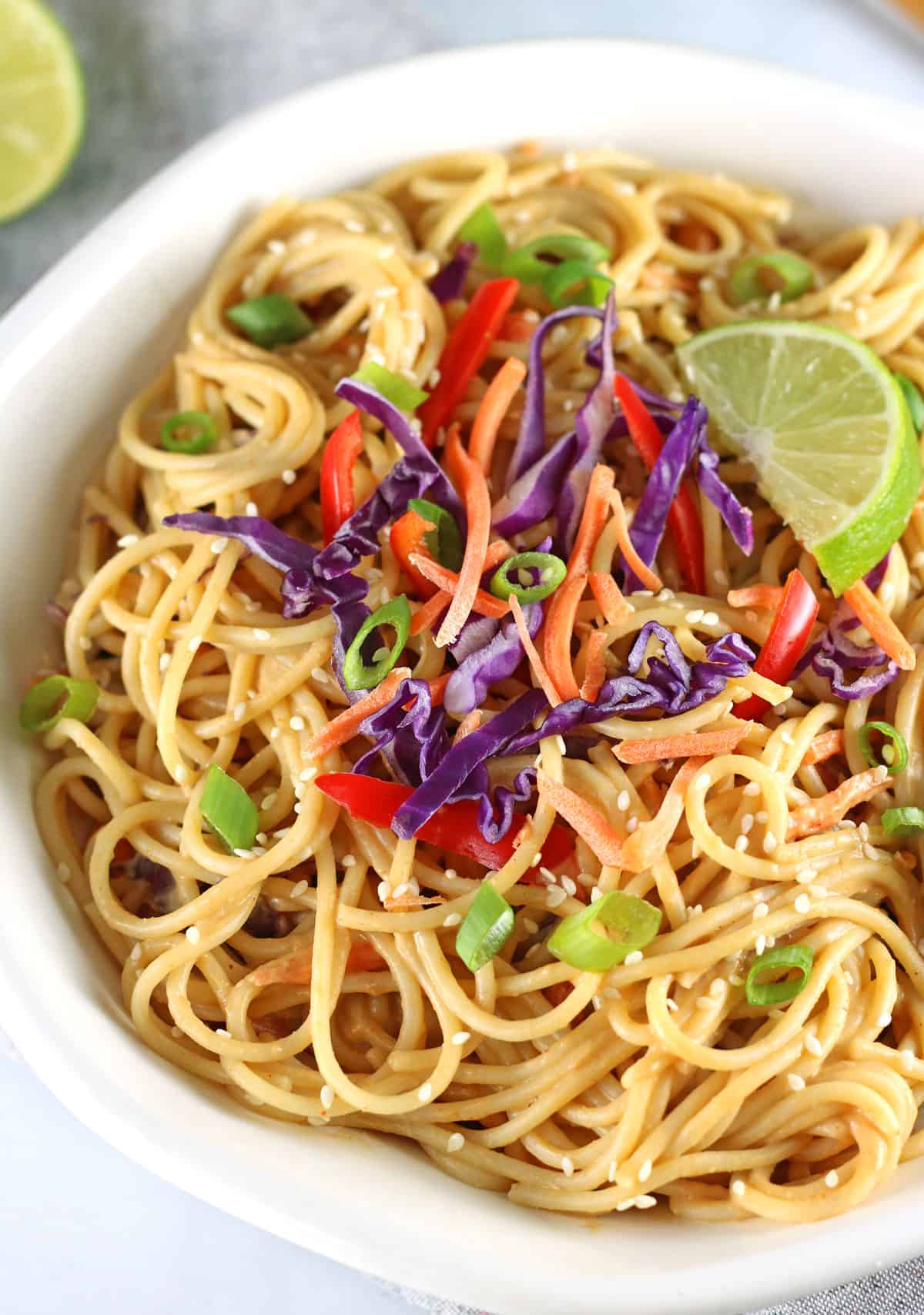 closeup of thai inspired spicy vegan peanut sauce noodles with veggies and a lime wedge.