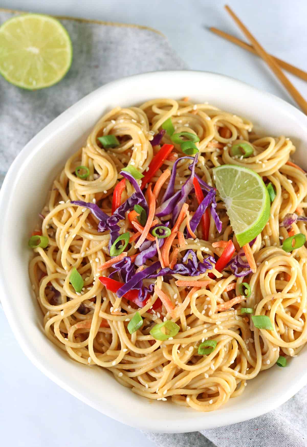 spicy peanut noodles with lime and chopsticks on grey napkin.