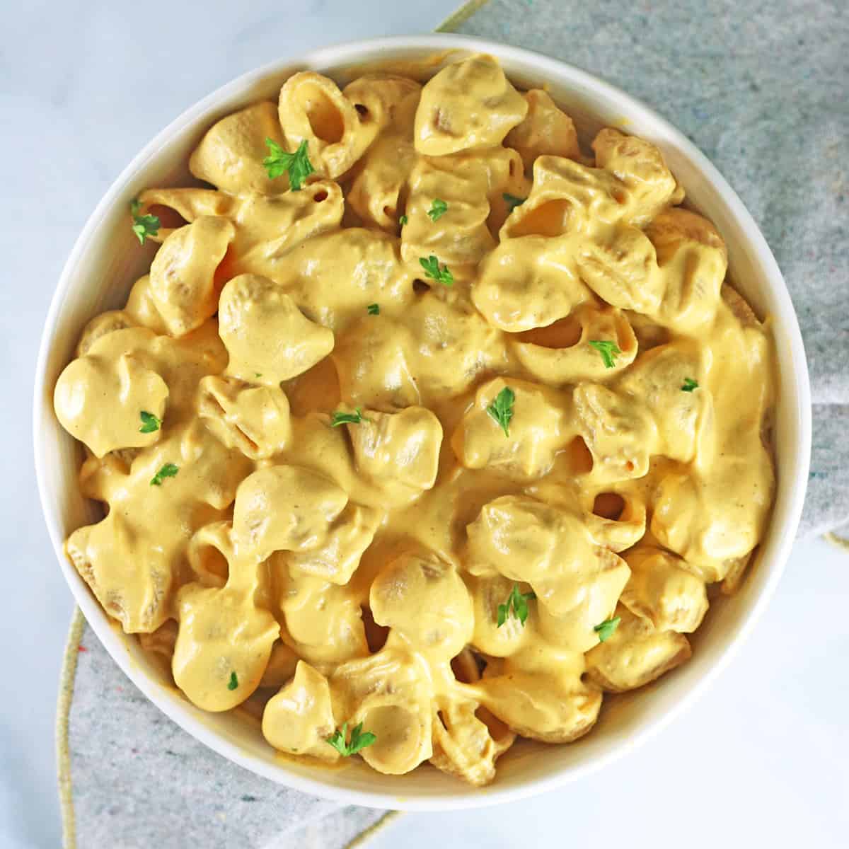 overhead shot of finished butternut squash mac and cheese in a white bowl garnished with fresh parsley.