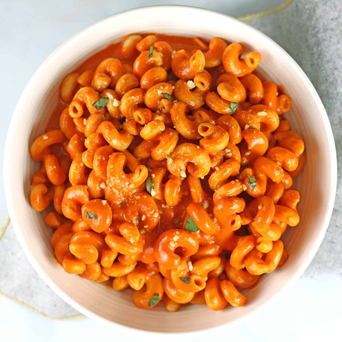 pasta with roasted red pepper sauce in a white bowl topped with fresh herbs and vegan parm.