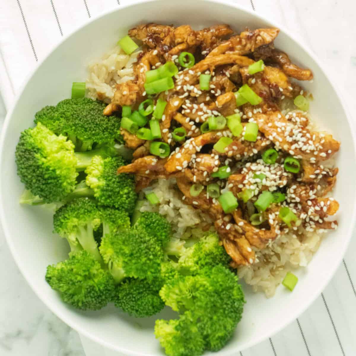 overhead shot of mongolian soy curls on a bed of brown rice with a side of steamed broccoli on a round white plate