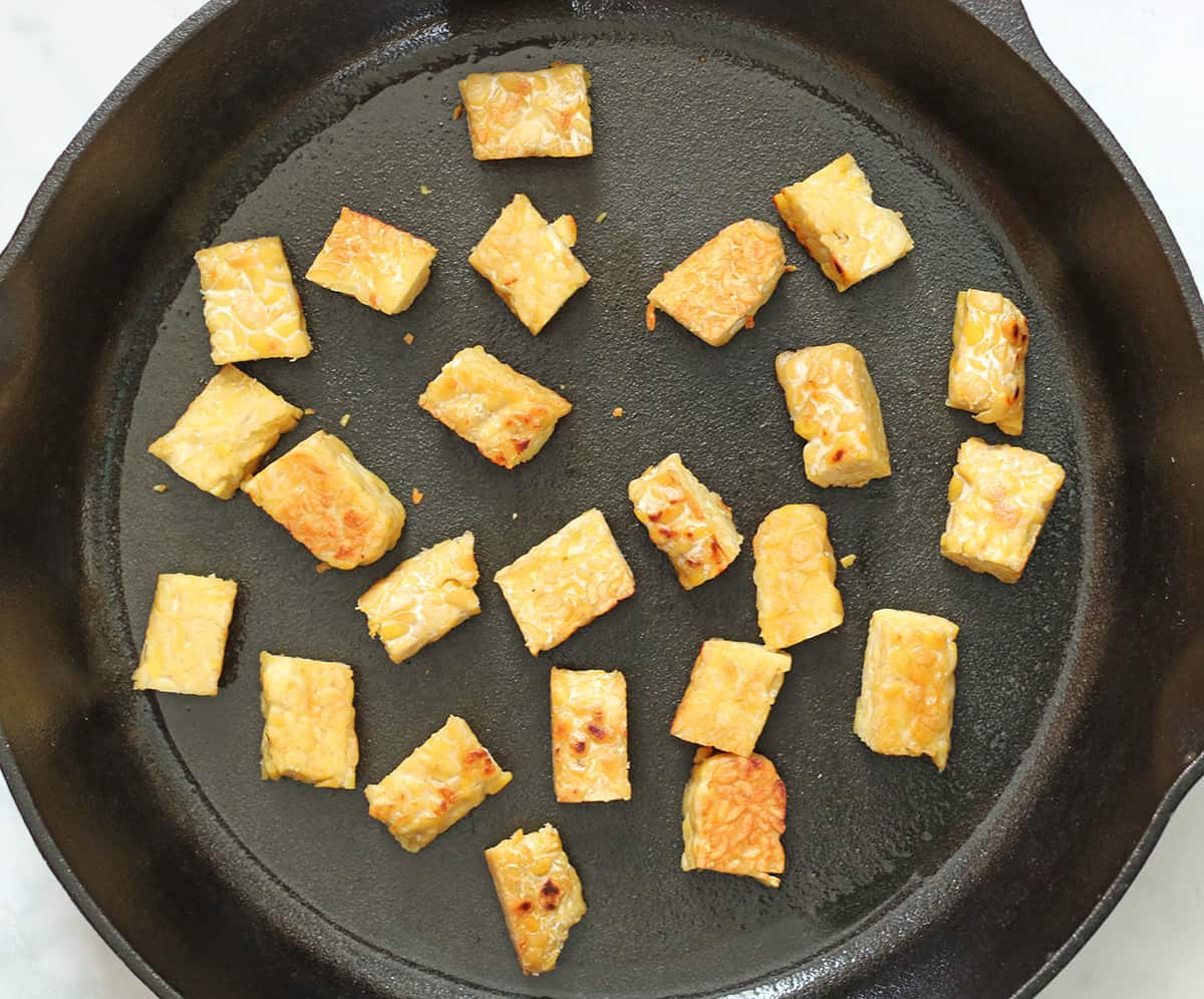 frying tempeh in a cast iron pan.