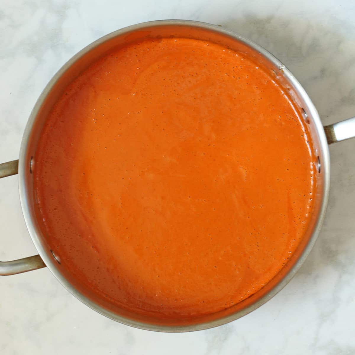 cooking creamy blended red pepper sauce in sauté pan.
