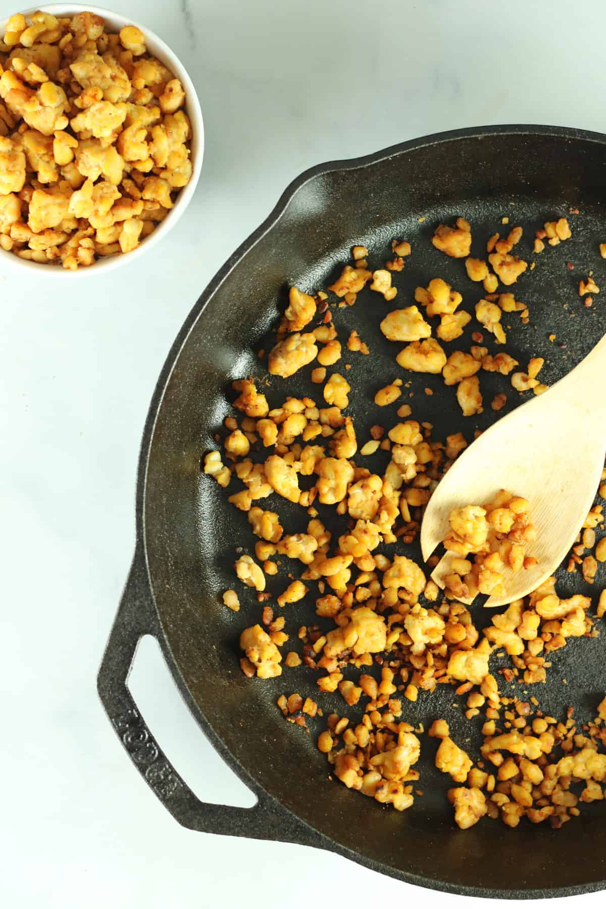 vegan meatless crumbles in skillet and white bowl with wooden spoon.