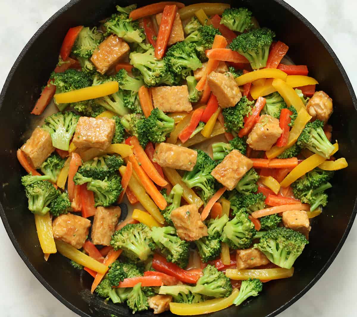 tempeh stir fry with veggies and peanut sauce in a cast-iron skillet.