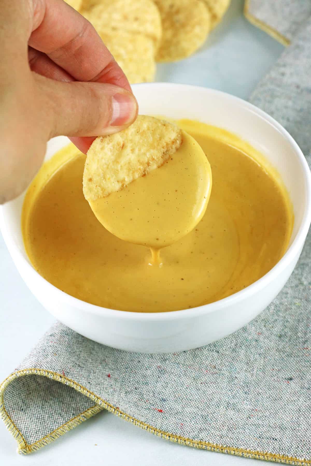 hand dipping chip into vegan nacho cheese sauce in a white bowl