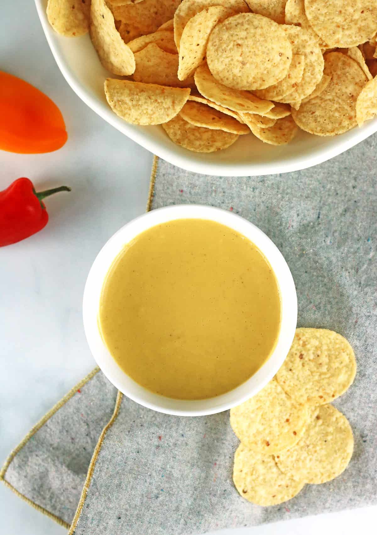 vegan nacho cheese sauce with tortilla chips in white bowls with peppers and gray napkin