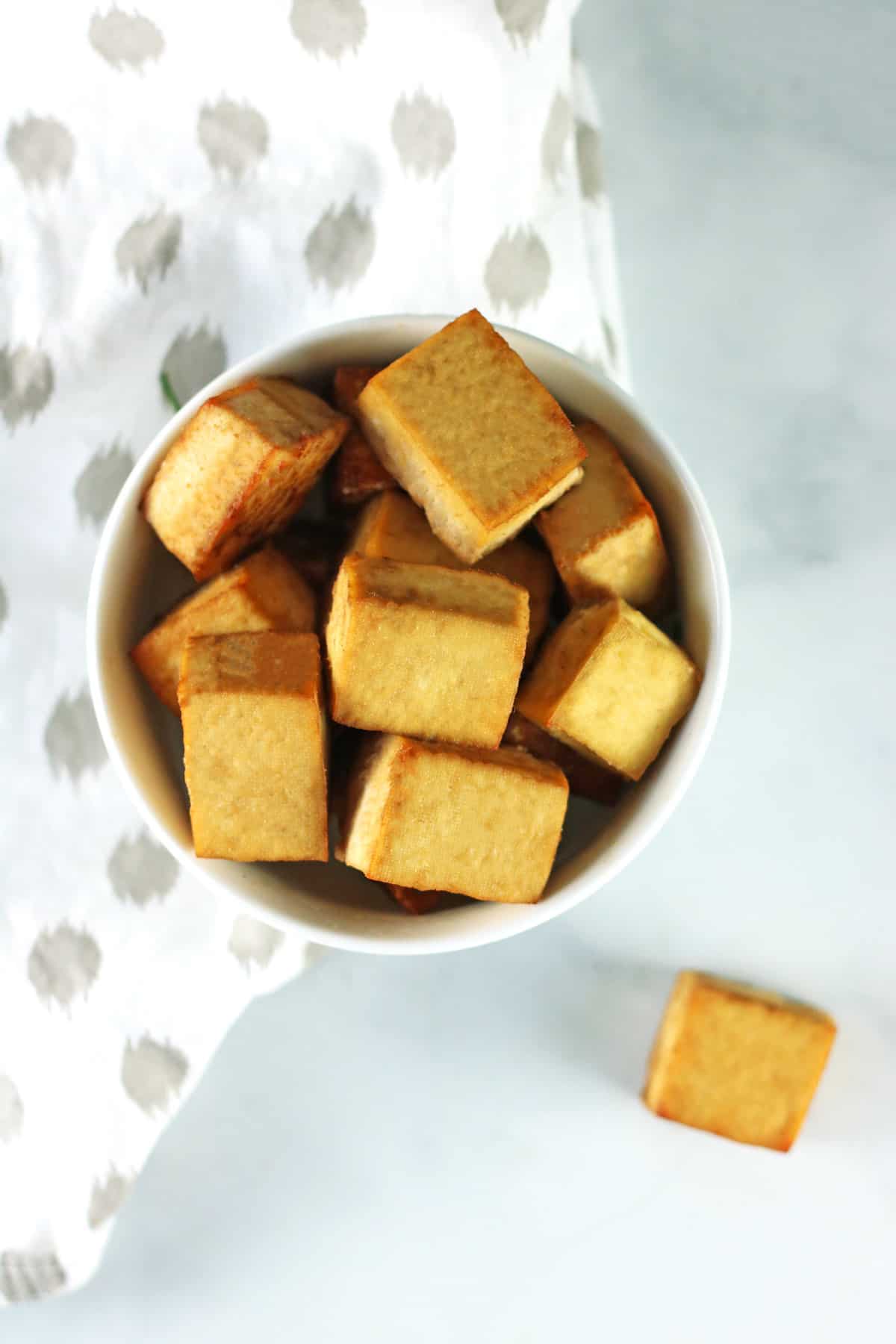 overhead shot of baked tofu in white bowl with white and gray napkin.