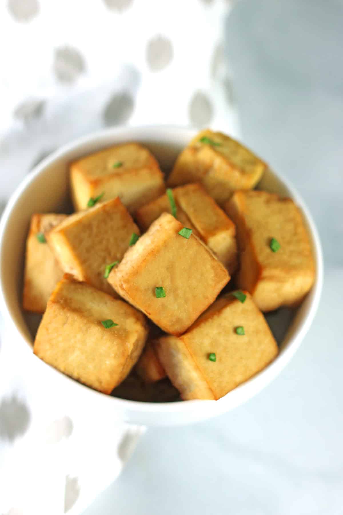 baked marinated tofu in white bowl with white and gray napkin.