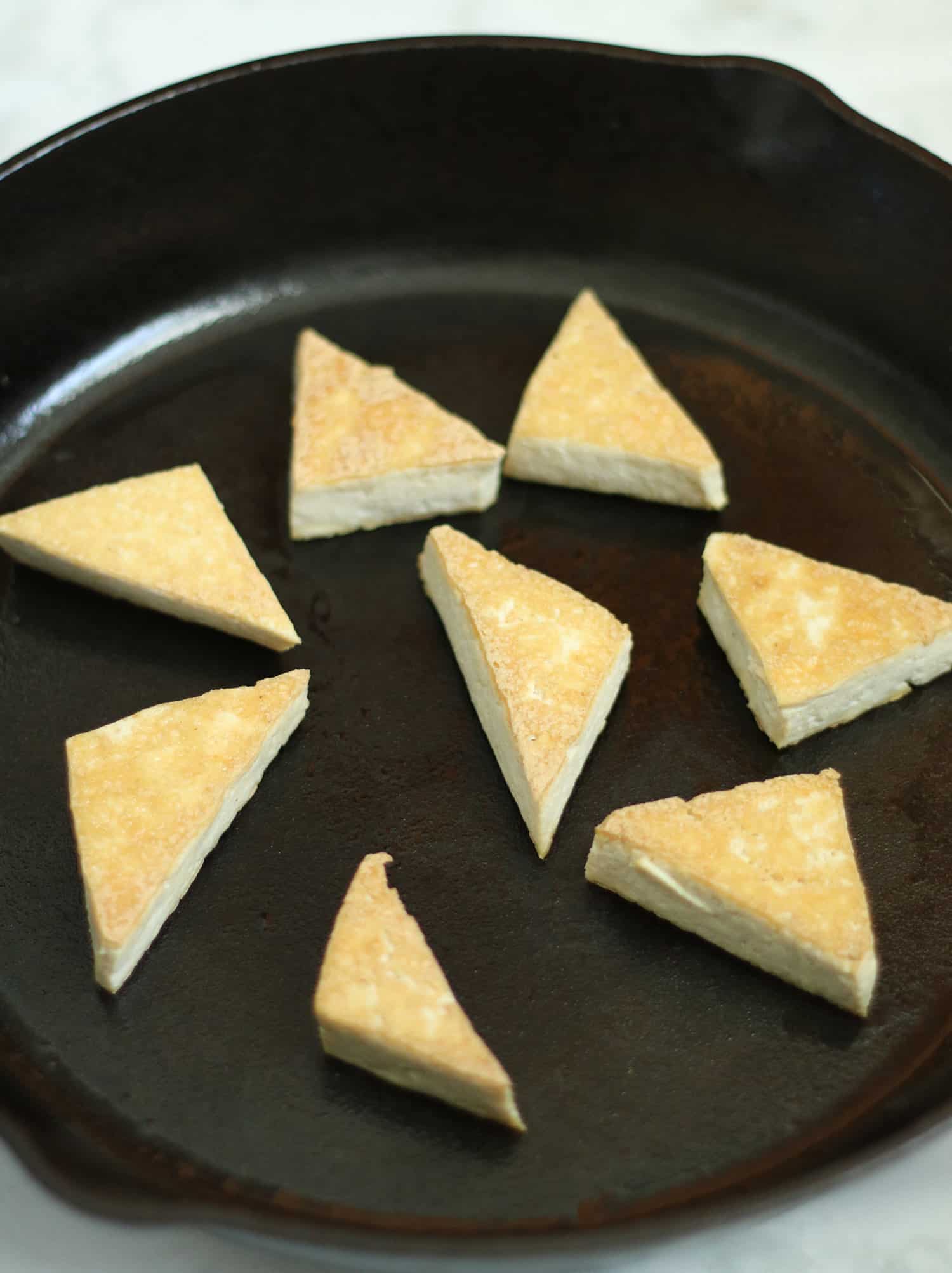 tofu triangles frying in cast iron skillet.