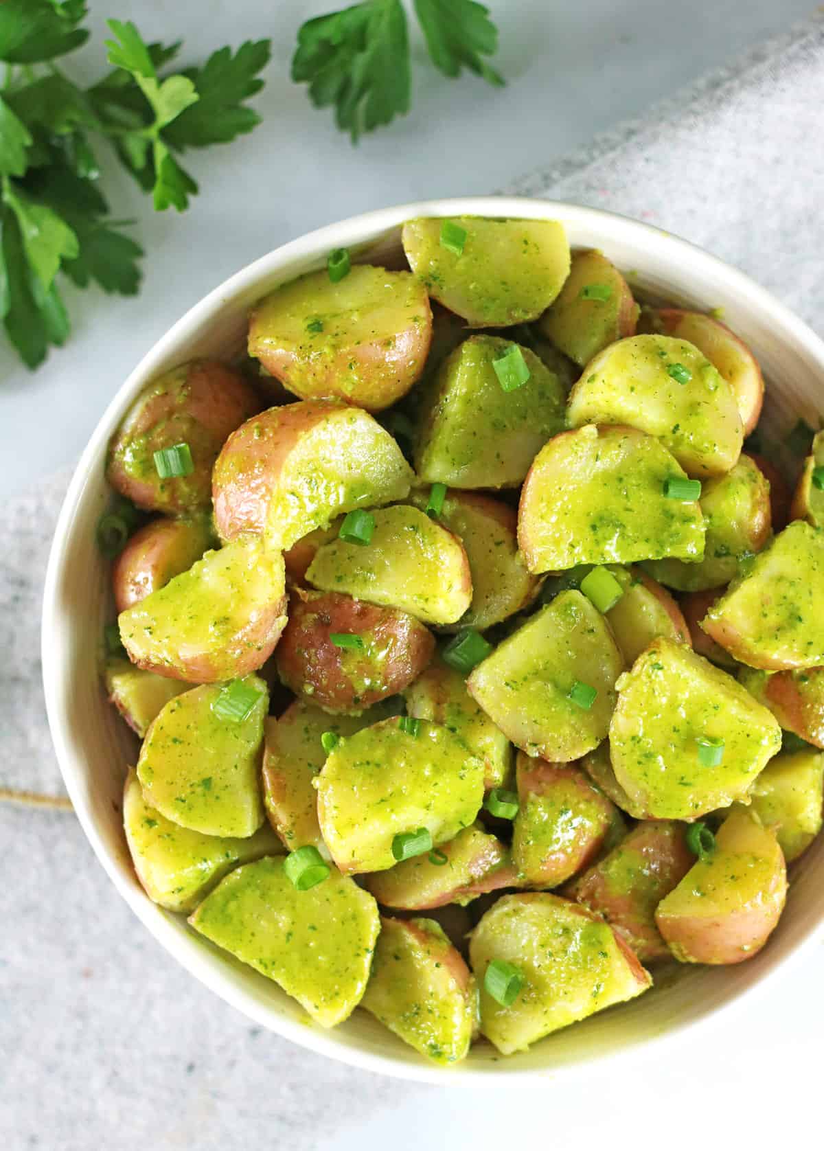 overhead of herbed potato salad in white bowl with fresh herbs