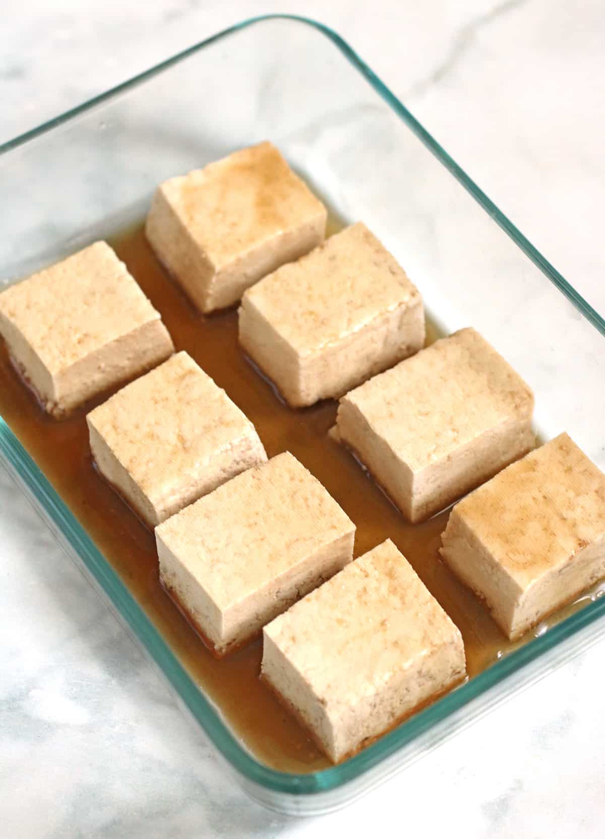 tofu squares being marinated in a glass bowl.