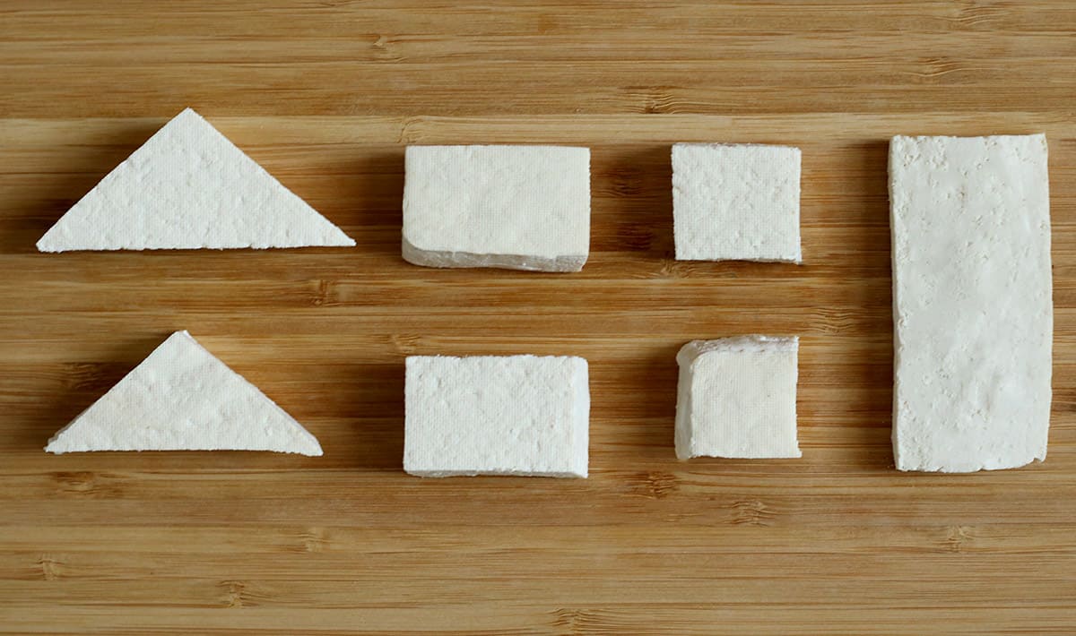 tofu cut into triangles, rectangles and squares on a wooden cutting board.