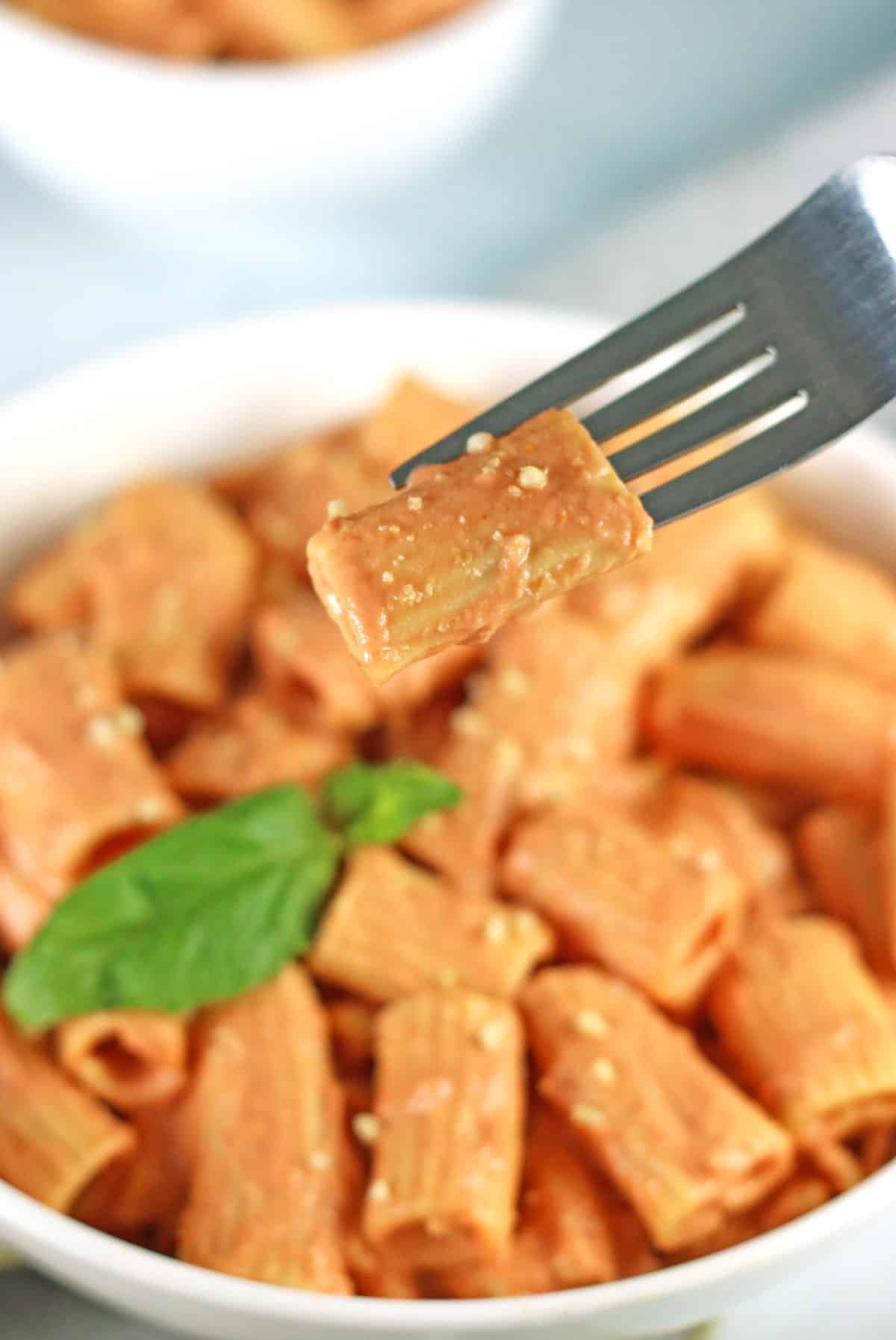 vodka sauce pasta on a fork with bowl of pasta in background.