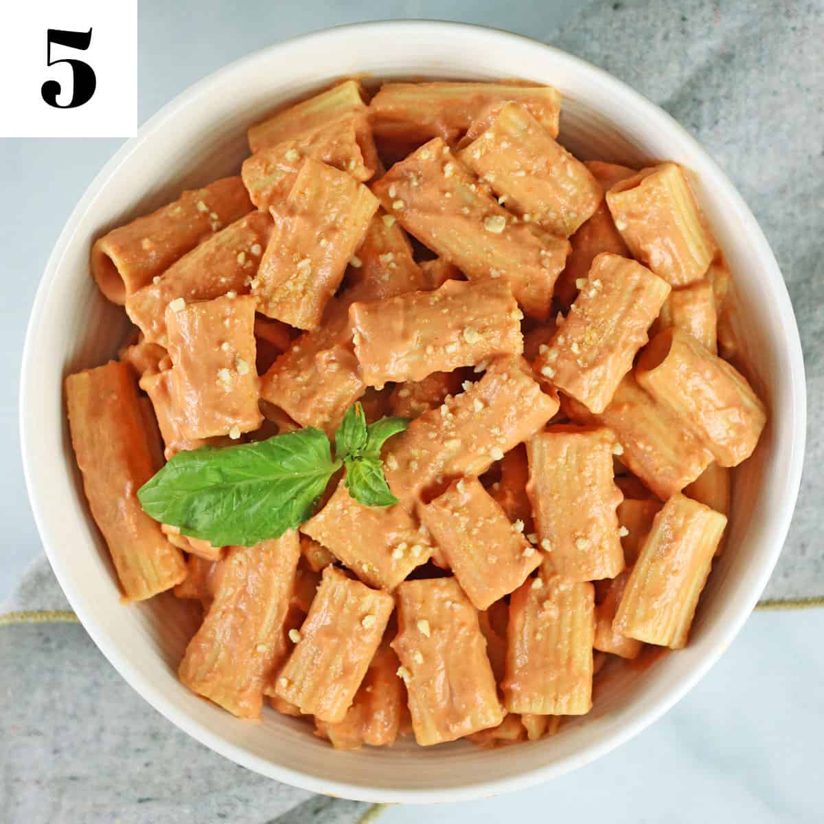 finished vegan vodka sauce pasta in a white bowl with a sprig of basil.