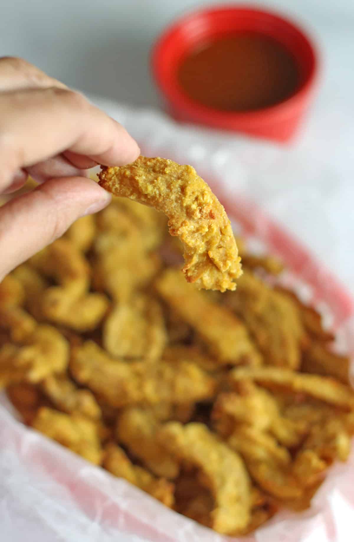 hand holding vegan chicken strip with more strips in background