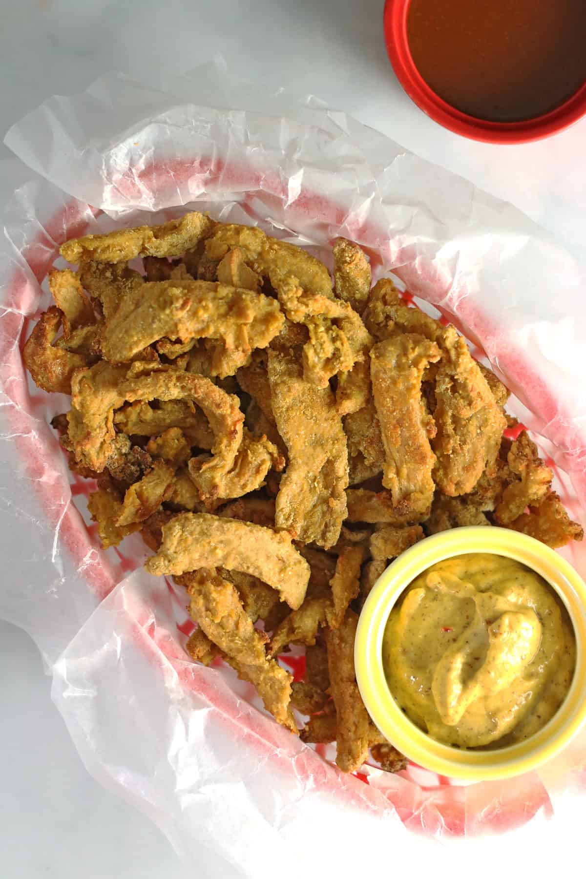 overhead shot of vegan chicken strips in a red basket with mustard and bbq sauce dips