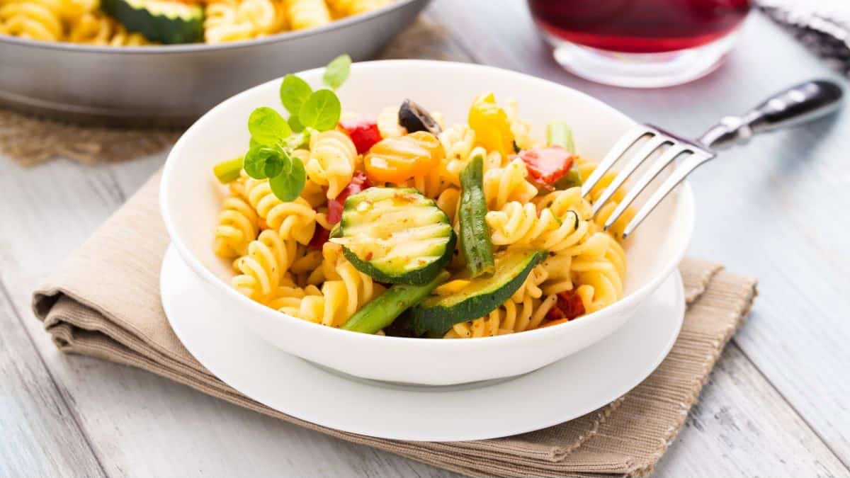 white plate and dish of pasta with veggies