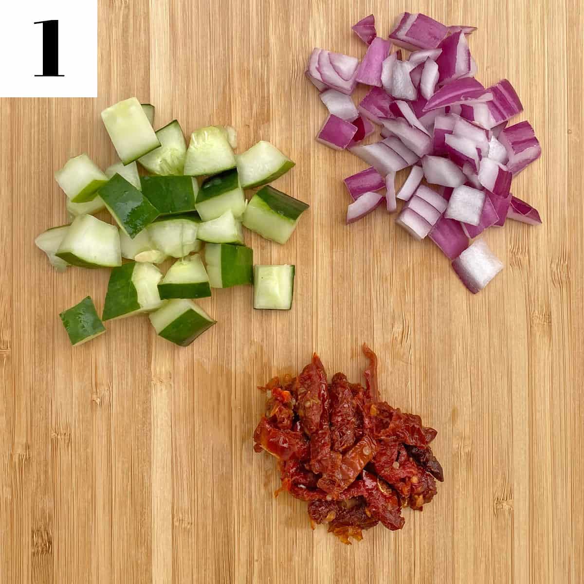 chopped cucumbers, sun-dried tomatoes, and red onion on a wooden cutting board