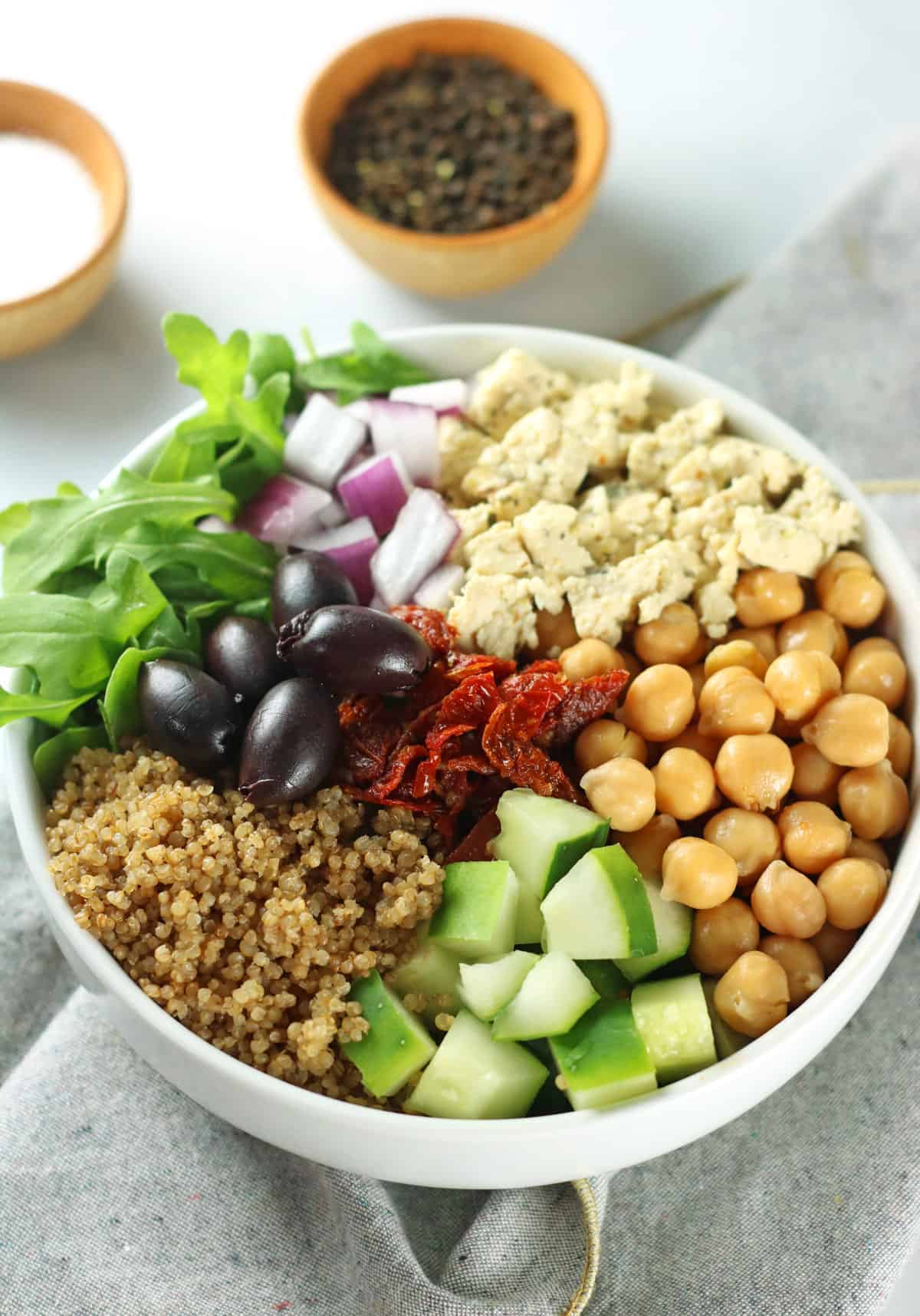 Greek Quinoa salad in bowl with chickpeas, quinoa, cucumber, olives, onions and arugula.
