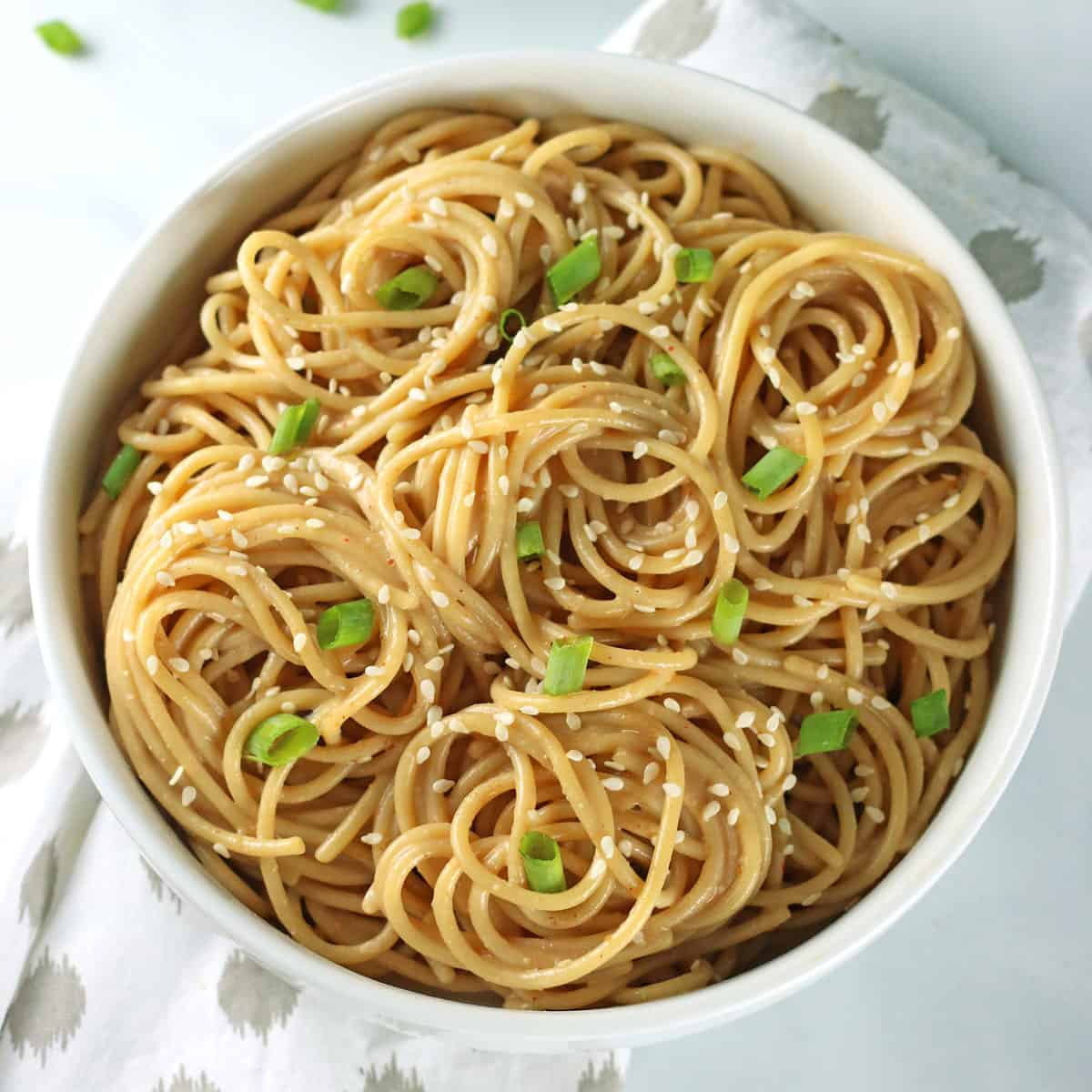 closeup of cooked garlic sesame ramen noodles in a white bowl garnished with scallions and white sesame seeds.