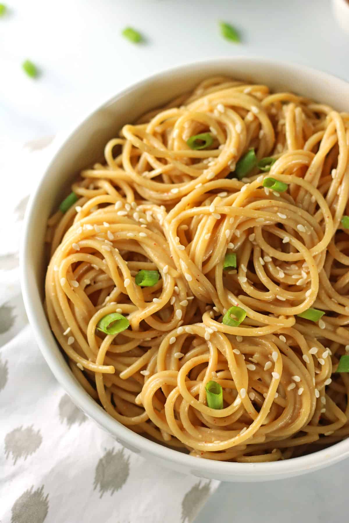 close up of bowl of garlic noodles with spicy peanut sesame sauce in white bowl.