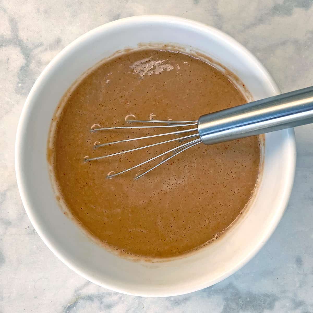 spicy garlic sesame noodle sauce in a white bowl with whisk.