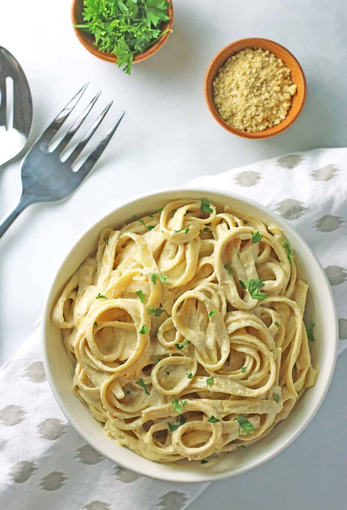 creamy vegan alfredo sauce pasta in white bowl with serving fork and napkin