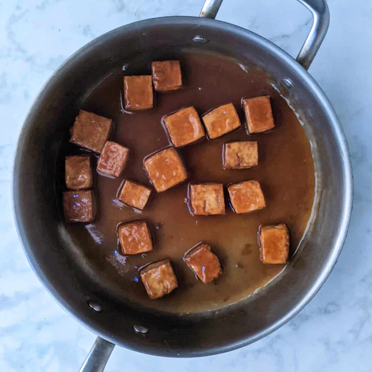 baked tofu tossed with sticky teriyaki sauce in large pan.