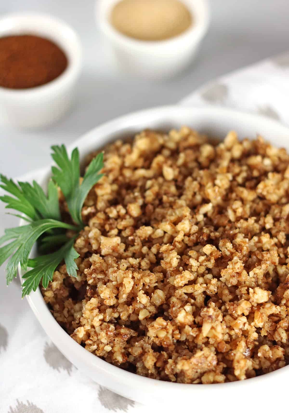 closeup of walnut taco meat in bowl with napkin and ramekins of chili and garlic powder.