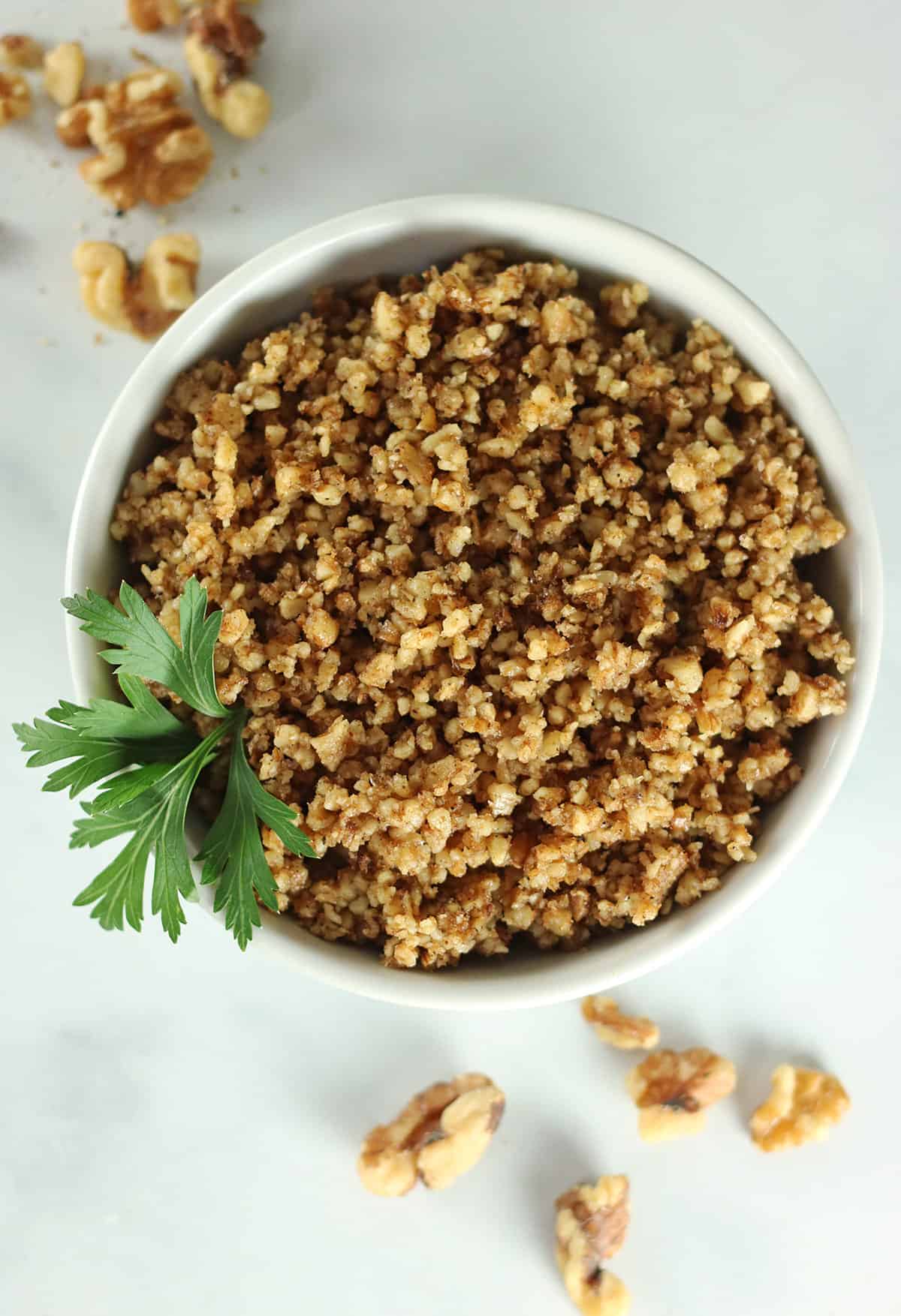 vegan walnut meat in white bowl with walnuts scattered around it.