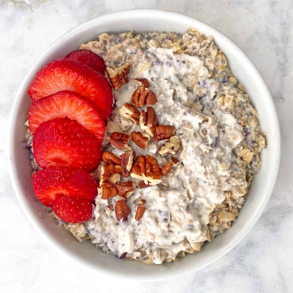 strawberry overnight oats with fresh strawberries, pecans, and yogurt in white bowl.